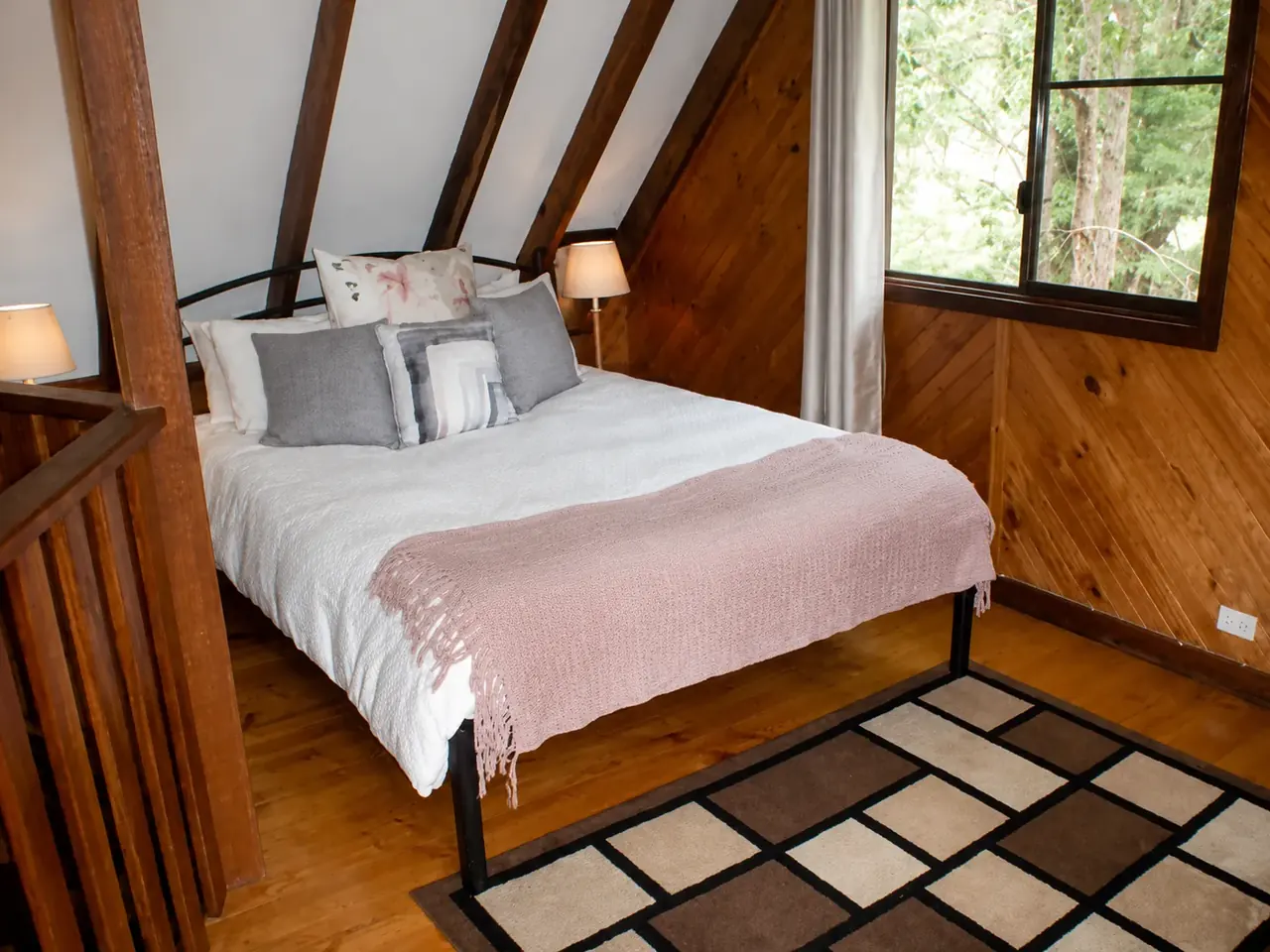 The queen bed on the mezzanine of a chalet, under the pitched timber roof
