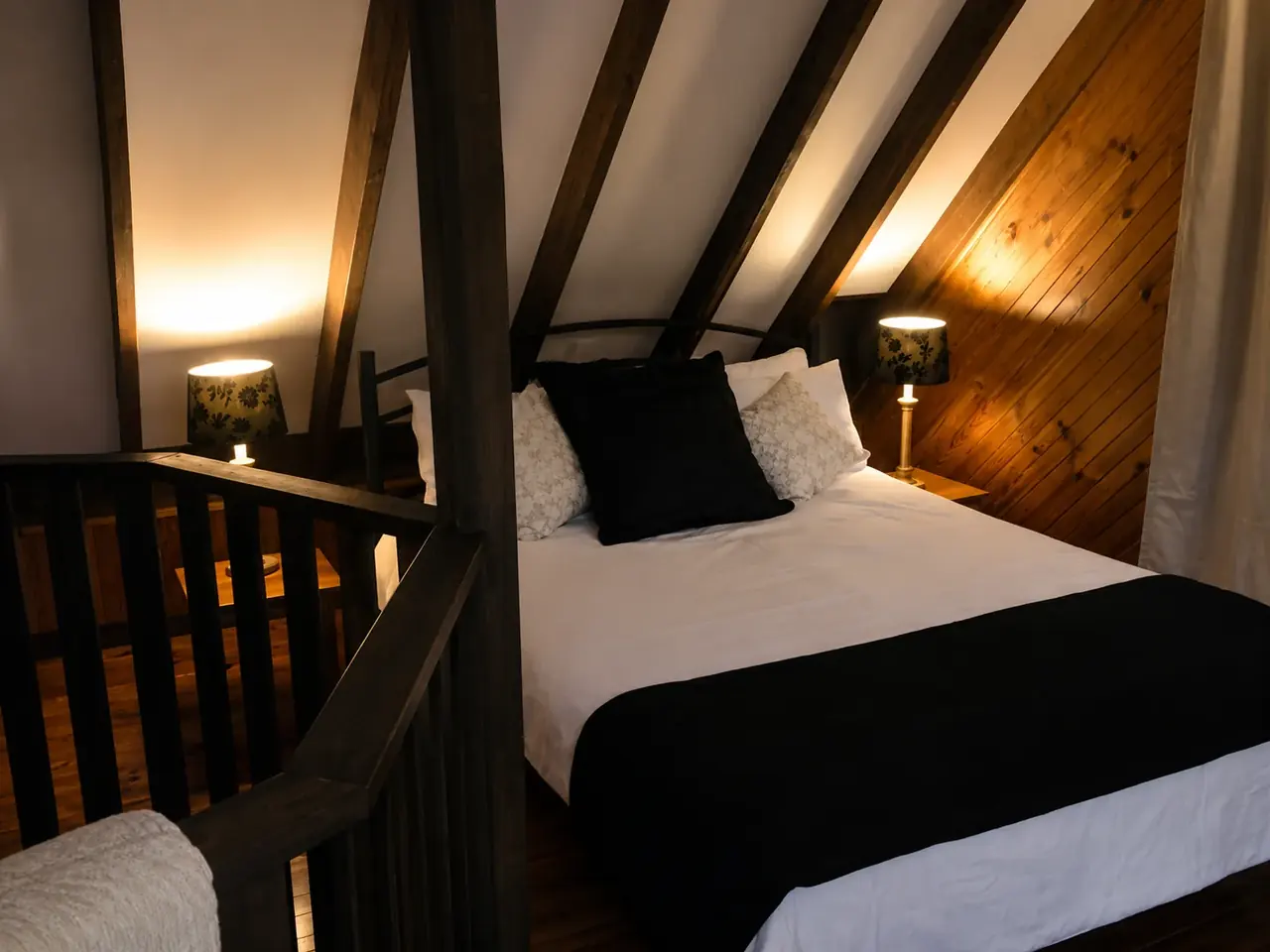 The mezzanine bedroom in a chalet, with a queen bed under the pitched timber roof