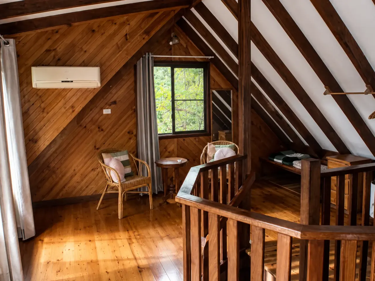 The timber interior of a chalet, with the staircase and a window onto the bush
