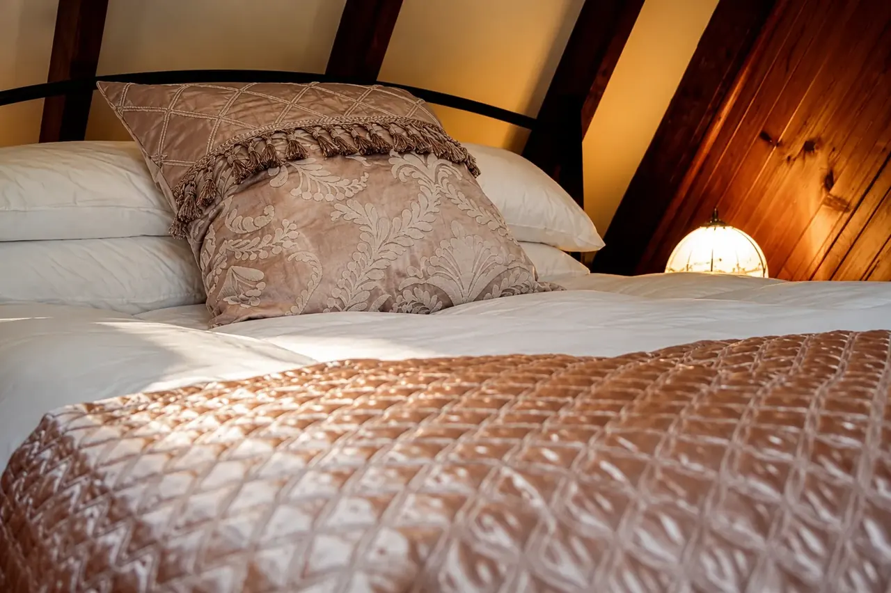 The mezzanine bed under the pitched timber roof, warm under lamplight