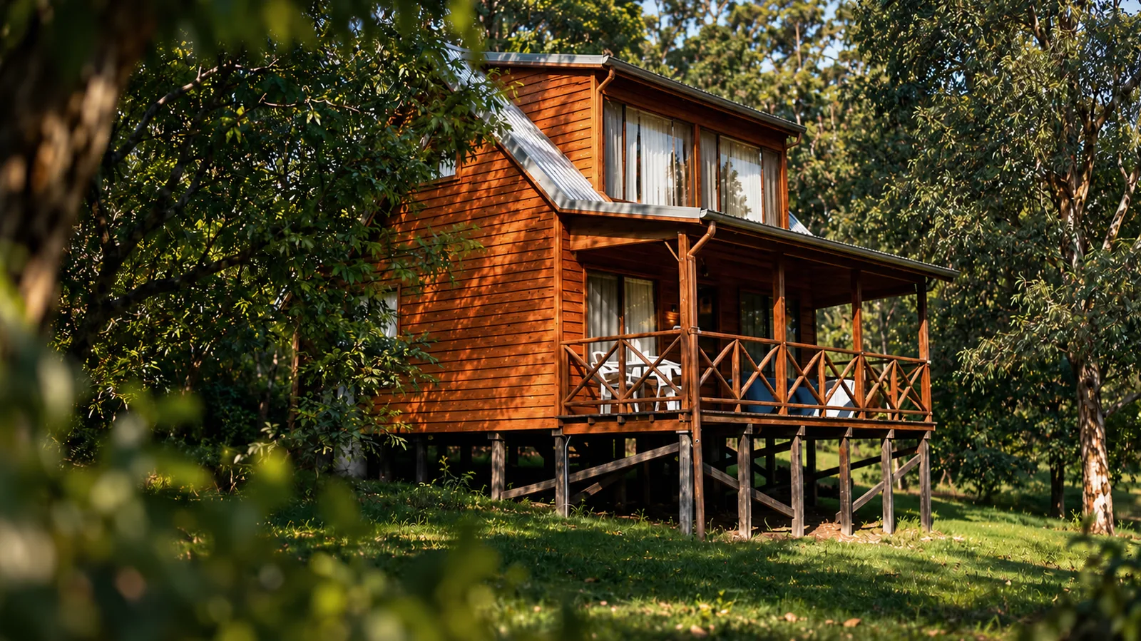 A timber spa chalet at Beyonderup Falls raised on stumps among sunlit gum trees on a green lawn