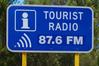 A roadside Tourist Radio 87.6 FM sign against the bush